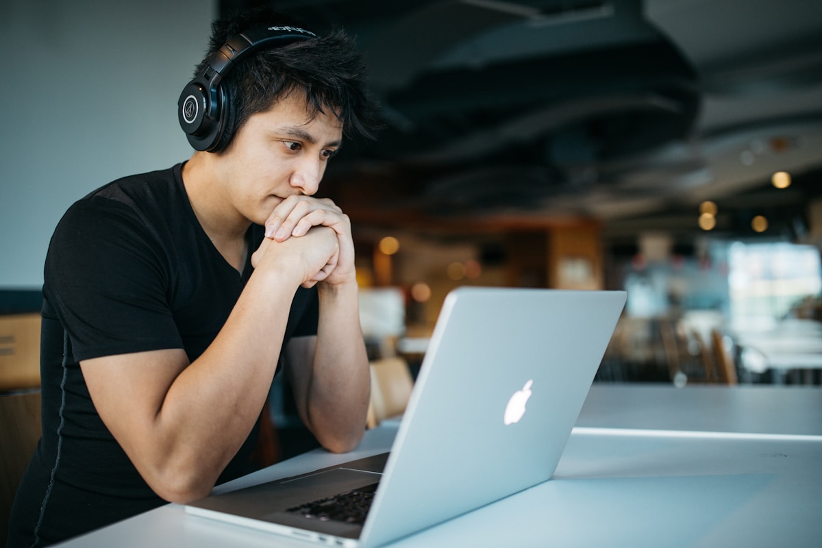 Cursos livres de programação que todo desenvolvedor deve conhecer man wearing headphones while sitting on chair in front of MacBook