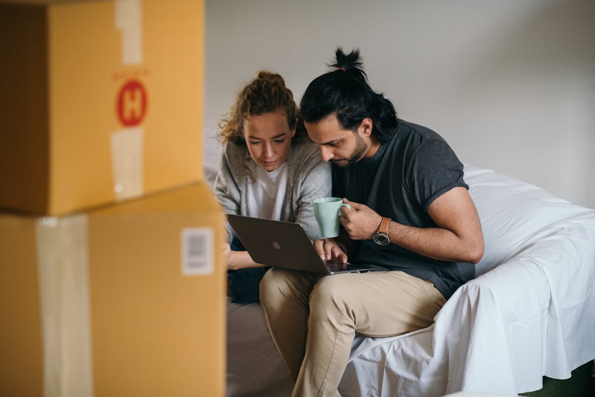 Algoritmos para análise de valorização imobiliária em cidades médias Couple surrounded by boxes checks laptop details on moving day.