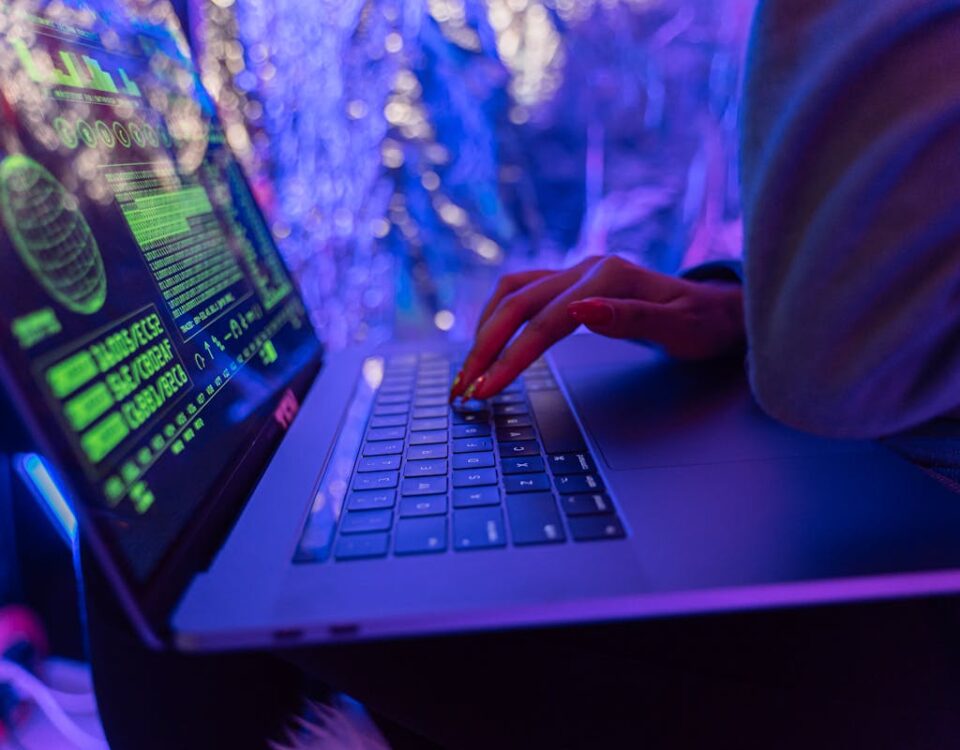 Firewall com IA: a nova era da segurança cibernética Close-up of hands typing on a laptop displaying cybersecurity graphics, illuminated by purple light.
