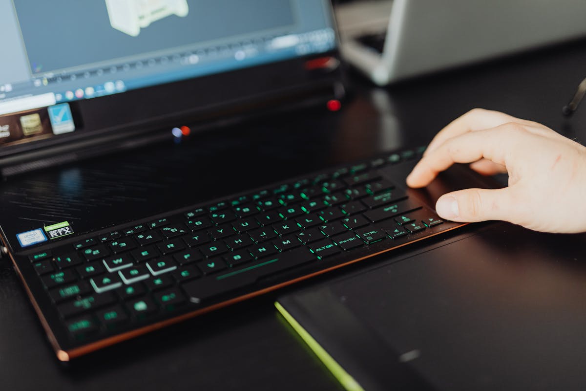 Close-up of a hand on a laptop keyboard working on a 3D modeling project with green LED keys.