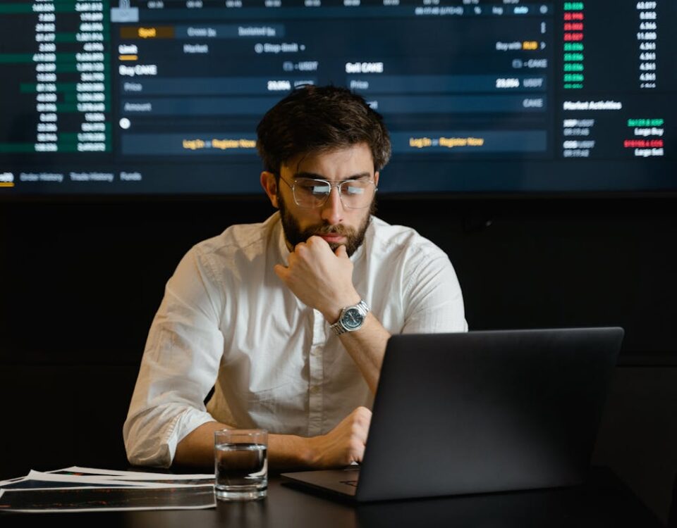 Algoritmos que ajudam no planejamento financeiro pessoal A man intensely analyzing stock market data on a laptop in an office setting.