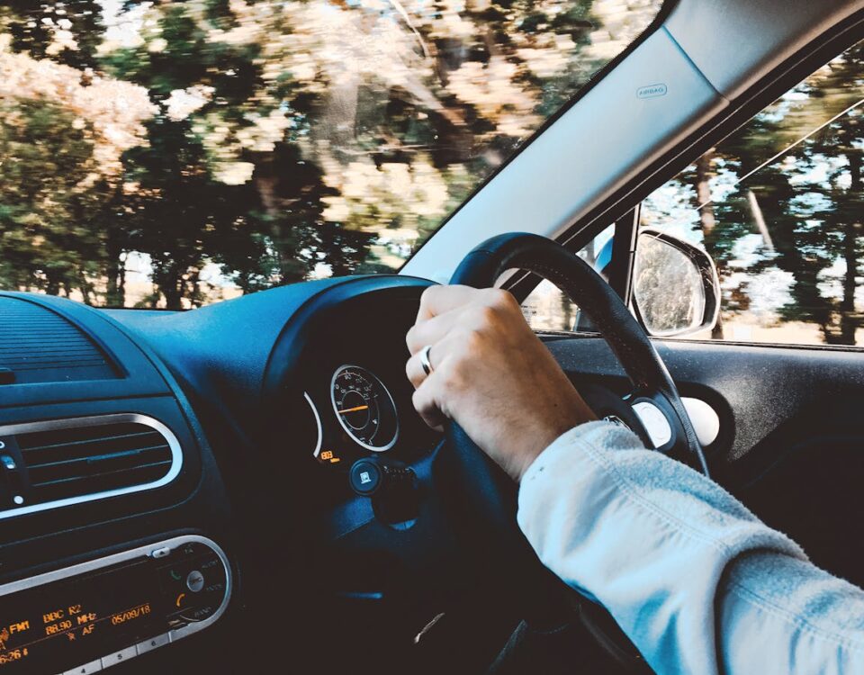 IA pode corrigir erros em treinos de direção autônomos? Driver's hand on steering wheel of a modern car during a daytime drive through scenic outdoors.