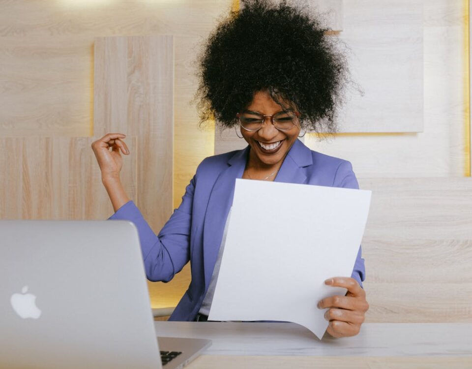 IA no apoio ao trabalho do auxiliar administrativo A cheerful woman celebrates her success at work, looking at a document in an office setting.