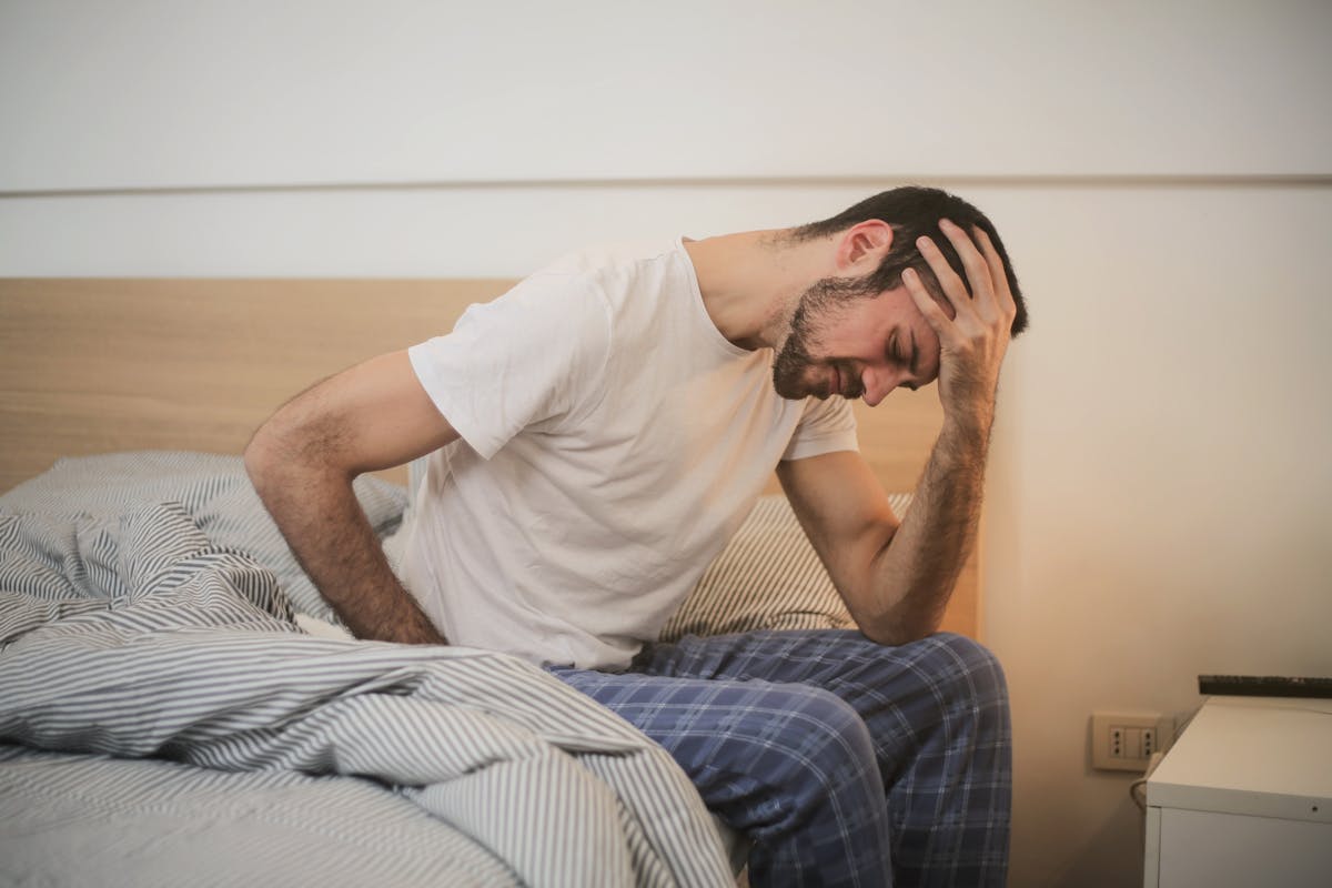 Inteligência artificial pode prever desconforto físico? A young man in pajamas holding his head, sitting on a bed, appears to be experiencing a headache.