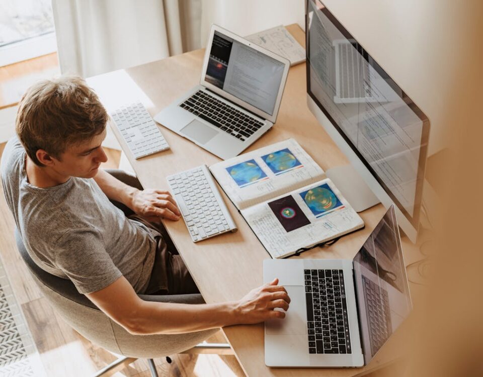 Algoritmos que ajudam a prever aprovação na prova prática A man multitasks with laptops and a desktop, coding in a home office setting.