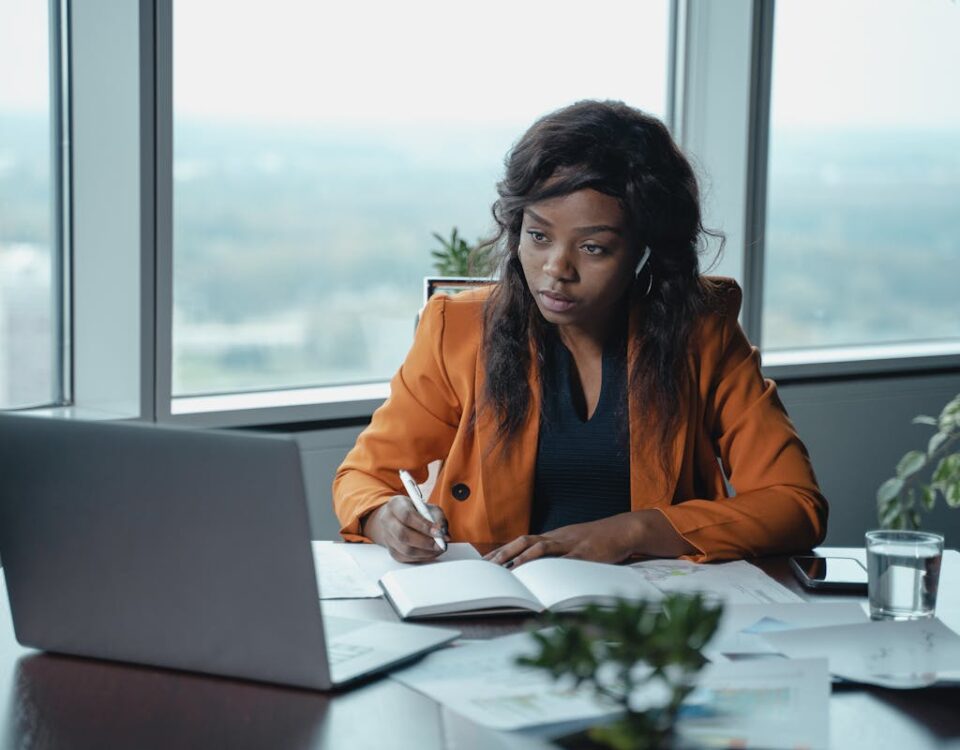 IA e seguros: Como a tecnologia transforma o setor? A businesswoman in a modern office intently working on a laptop and writing in a notebook.