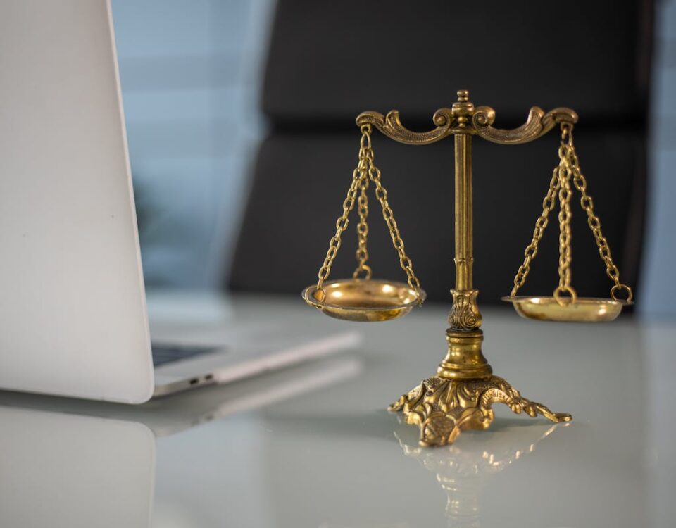 IA na defesa criminal: O futuro dos advogados criminalistas Golden justice scales on a desk beside a laptop, symbolizing law and balance.