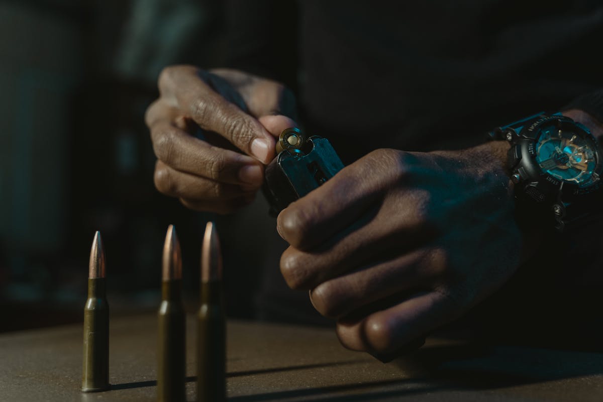Inteligência artificial em sistemas de armas modernas Detailed shot of hands loading a weapon magazine, surrounded by bullets, showcasing precision and focus.
