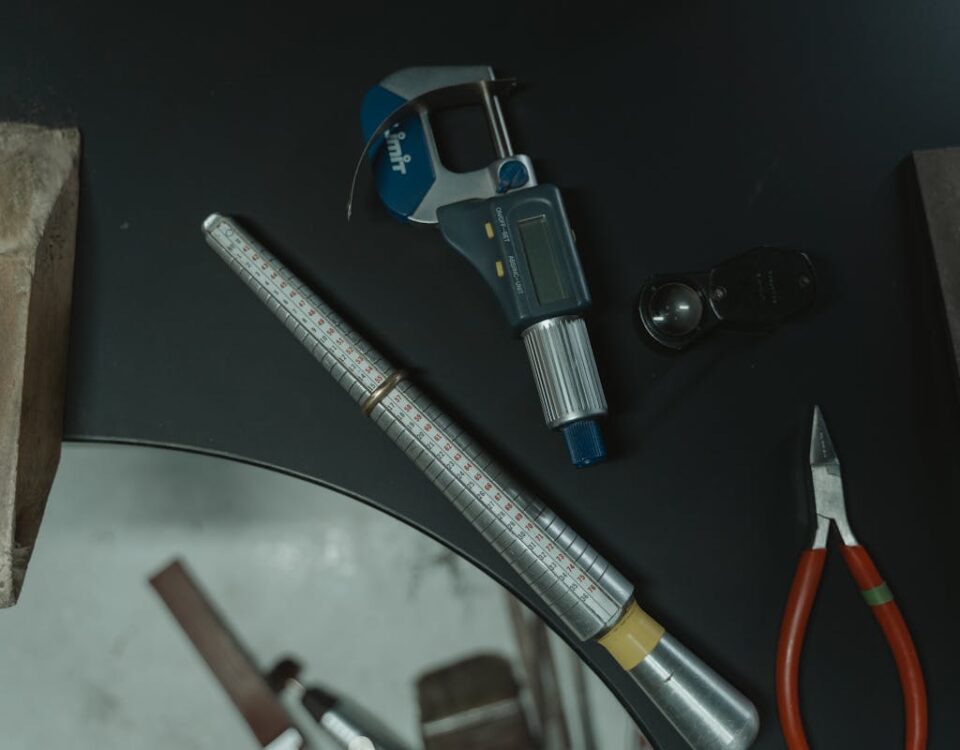 A collection of jewelry crafting tools including a ring mandrel and caliper on a workbench.