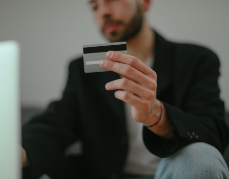 Inteligência artificial pode agilizar crédito para negativados? Blurred image of a man holding a credit card, emphasizing online shopping.