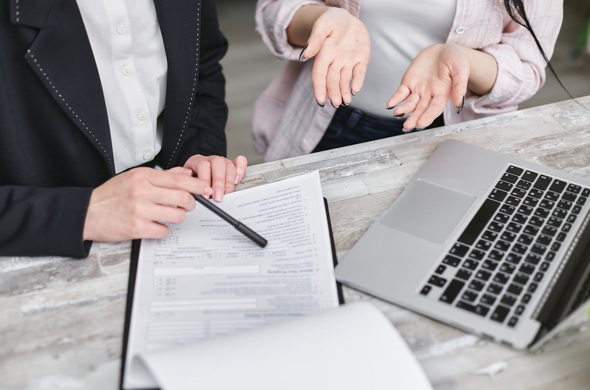 IA nas corretoras de seguros: Como isso funciona? Two professionals discussing a contract at a business meeting with documents and a laptop.