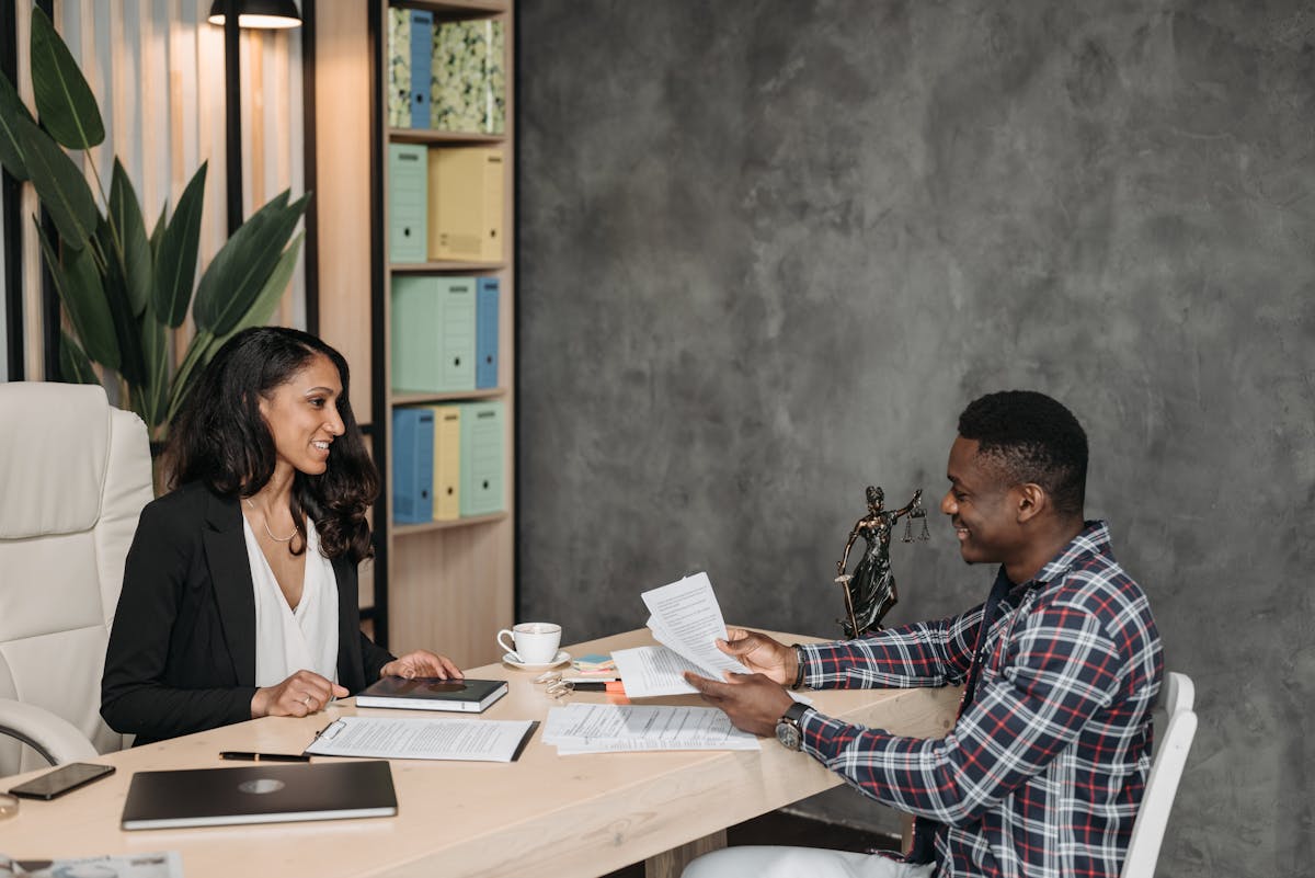 IA identifica advogados especialistas em planos de saúde Two professionals having a discussion in a stylish office with paperwork and a laptop.