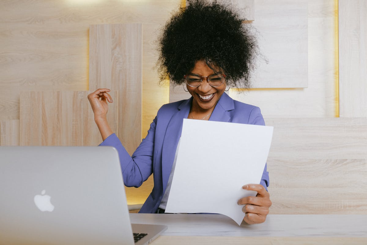 IA na formação de motoristas: O futuro da CNH A cheerful woman celebrates her success at work, looking at a document in an office setting.