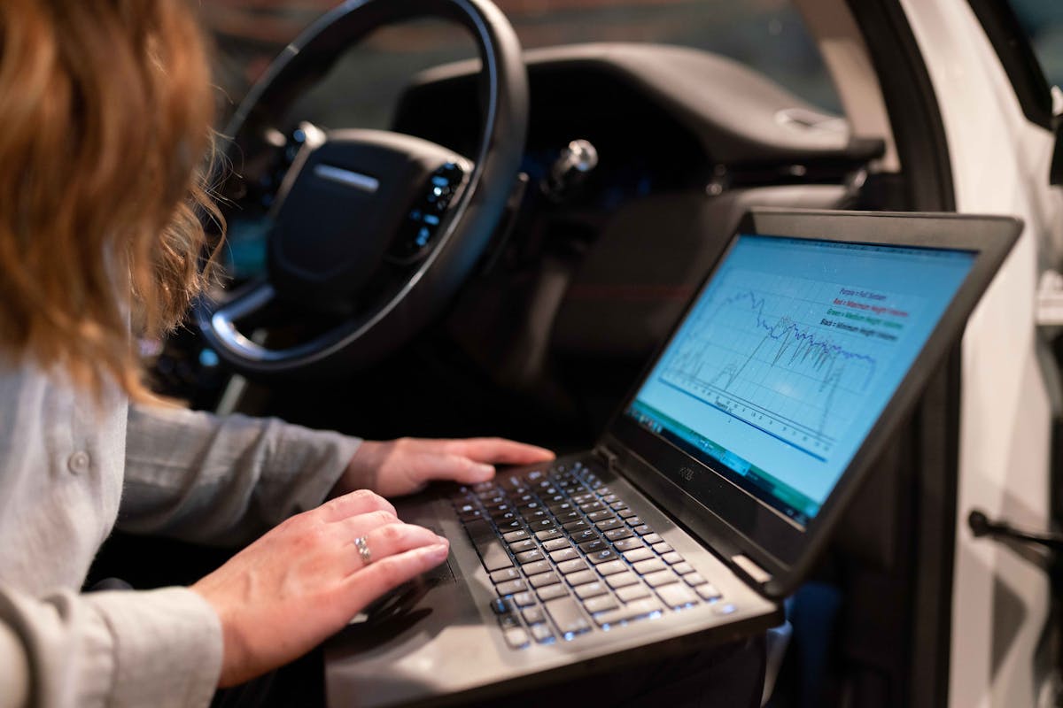 Redes neurais treinando carros para dirigir em cidades reais Female engineer using laptop to analyze vehicle data inside a car for testing purposes.
