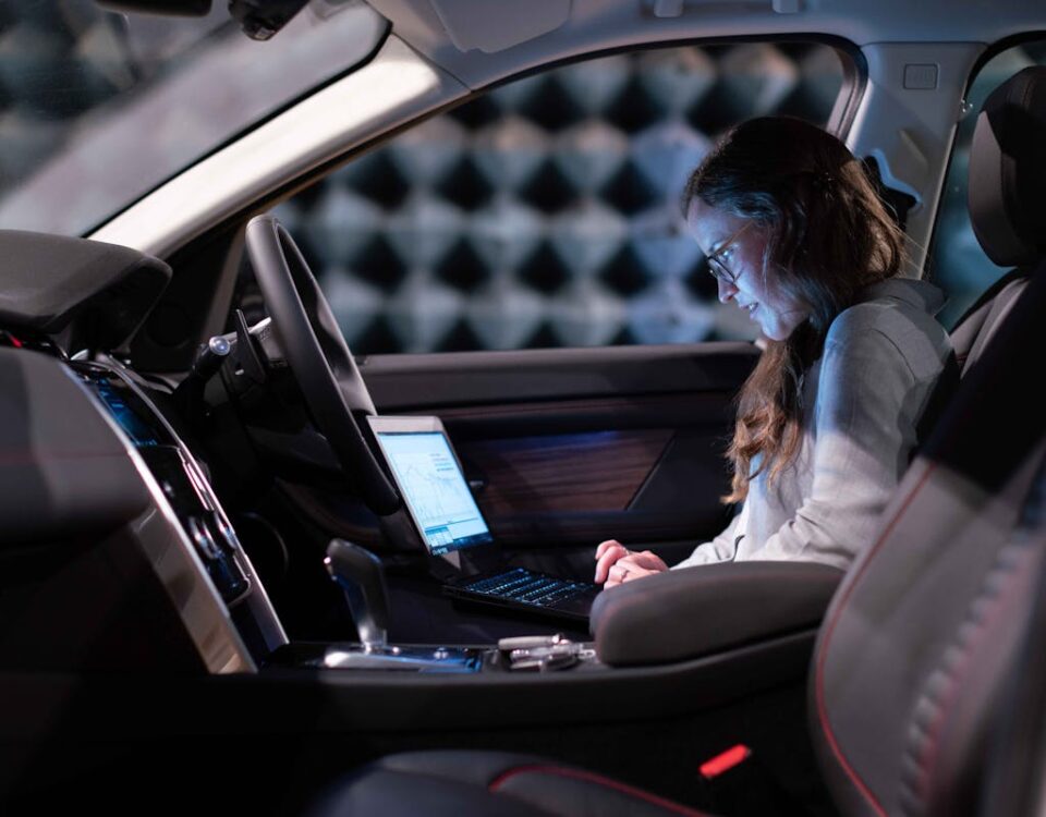 Redes neurais treinando carros para dirigir em cidades reais Woman working on a laptop inside a car, testing sound engineering in an isolated chamber.