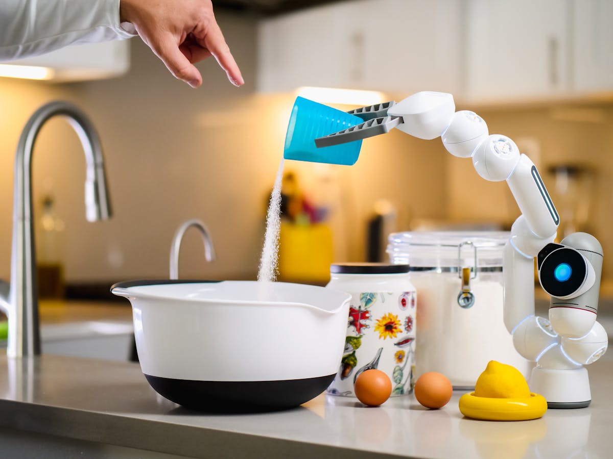 A robot arm assists in baking by pouring ingredients into a mixing bowl in a modern kitchen.
