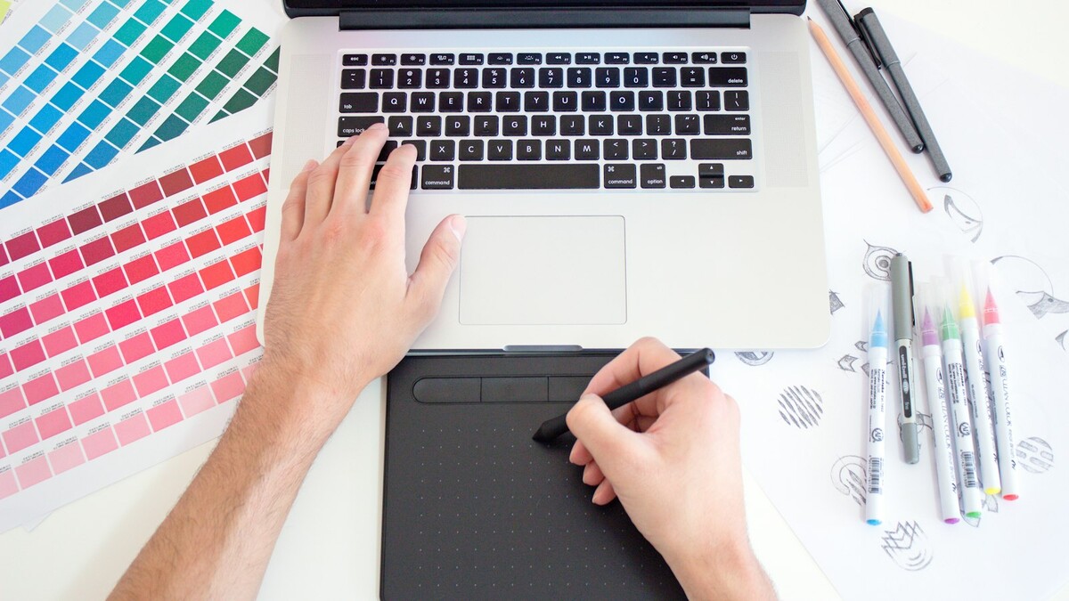 Designer desenhando em mesa digitalizadora ao lado de amostras de cores