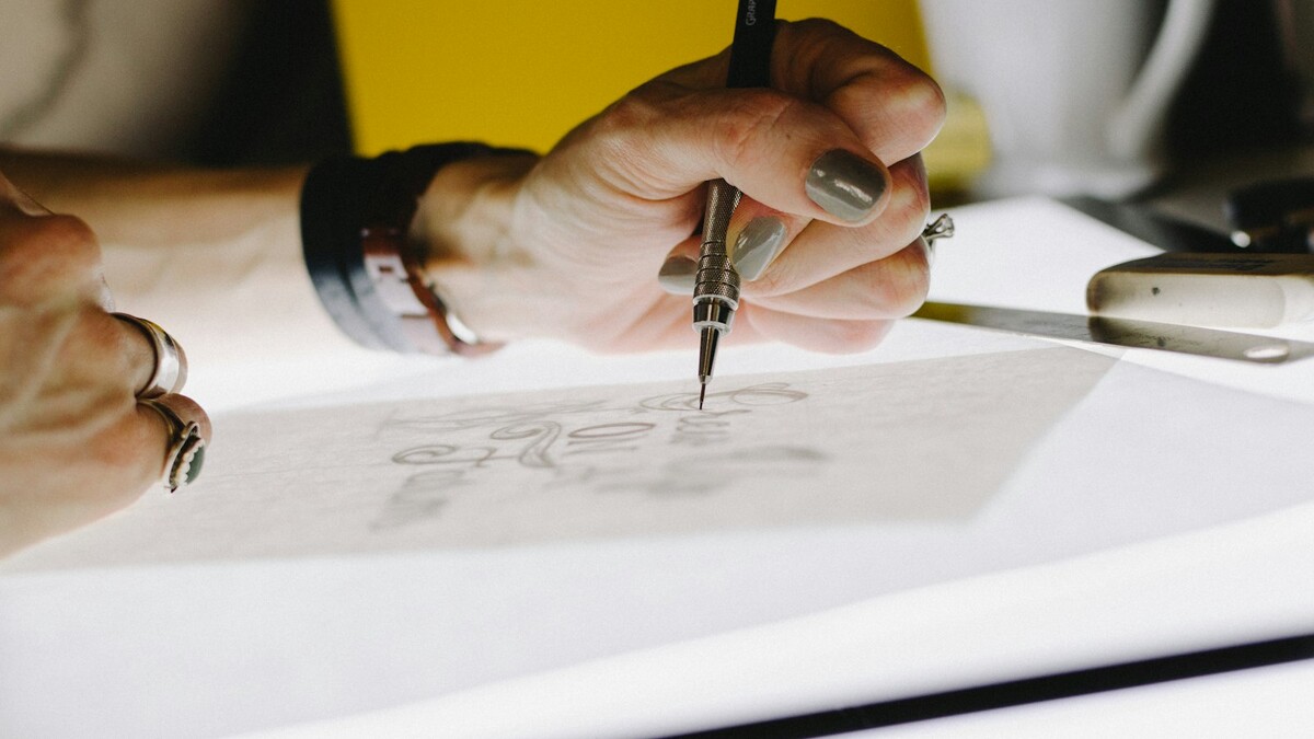 Mão desenhando letras com lapiseira em papel vegetal