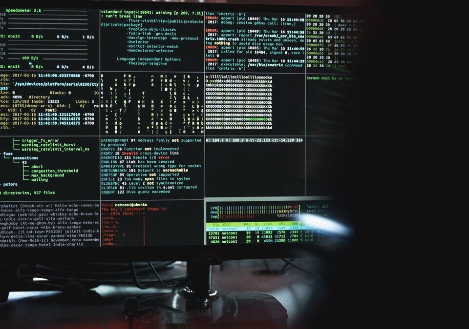 Monitor com várias janelas de terminal e código em ambiente escuro