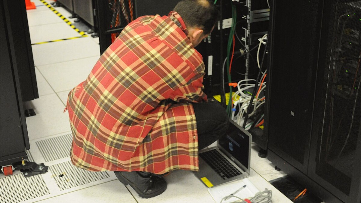 Técnico agachado com notebook conectado a um rack de servidores em data center